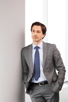 Portrait of handsome businessman standing near windows in office