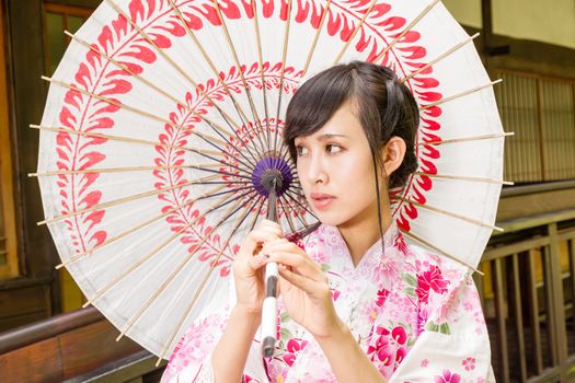 Asian woman wearing a kimono in front of  Japanese house holding umbrella