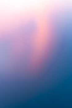 Sunset colored clouds reflecting in calm water abstract background colors transition pale pink through beep blue diagonally.