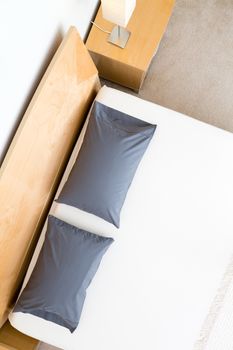 King size bed viewed from above with black pillows, a wooden headboard and bedside cabinet over a neutral beige carpet, in an interior decor concept