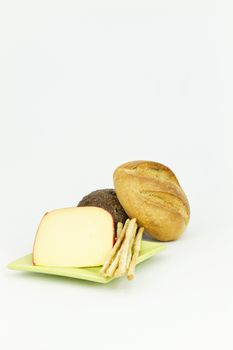 Vertical image with dark and light breads placed with gouda cheese and breadsticks on white background.