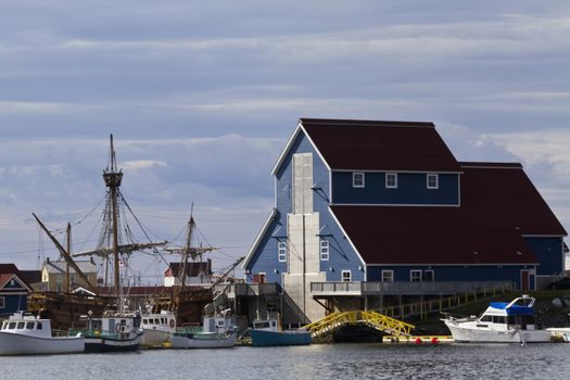 Maritime view of Bonavista Harbour, replica of John Cabot's ship the Matthew visible, and the Matthew Legacy Interpretation Center as the skyline's central building.  Location is town of Bonavista in the province of Newfoundland and Labrador in Canada.  
