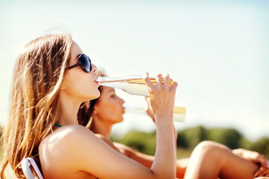 summer holidays and vacation - girls in bikinis with drinks on the beach chairs