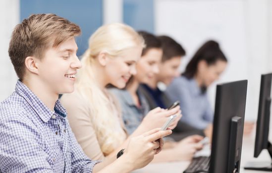 education, technology and internet concept - students with computer monitor and smartphones