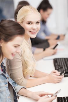 education, technology and internet concept - students with computer monitor and smartphones