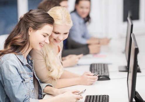 education, technology and internet concept - students with computer monitor and smartphones