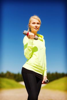 sport and lifestyle - young sporty woman with light dumbbells outdoors