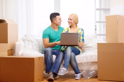 moving, home, technology and couple concept - smiling couple relaxing on sofa with laptop in new home