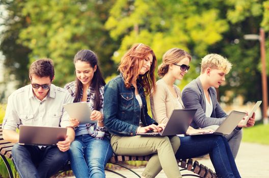 summer, internet, education, campus and teenage concept - group of students or teenagers with laptop and tablet computers hanging out