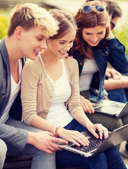 summer, internet, education, campus and teenage concept - group of students or teenagers with laptop computers hanging out