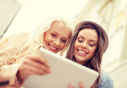 holidays, technology and tourism concept - two beautiful girls toursits looking into tablet pc in the city