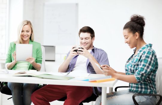 education, technology and internet - students looking into phones and tablet pc at school