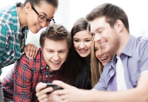 education and internet concept - smiling students looking at smartphone at school