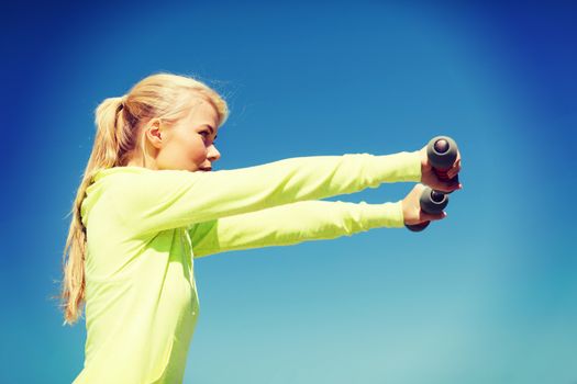 sport and lifestyle - young sporty woman with light dumbbells outdoors