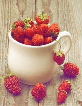 White Tea Cup Full of Fresh Ripe Forest Strawberries closeup on Rustic Wooden background. Retro Styled