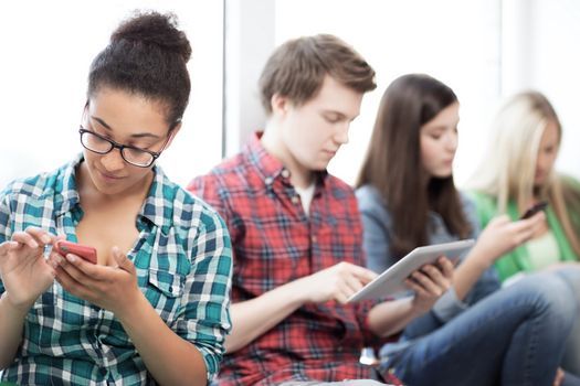 technology and internet concept - students looking into phones and tablet pc at school