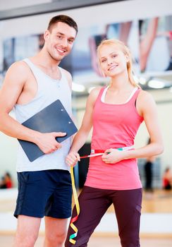 fitness, sport, training, diet, gym and lifestyle concept - two smiling people with clipboard and measure tape in the gym