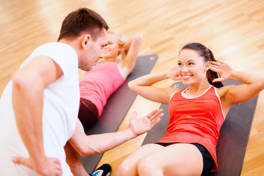 fitness, sport, training, gym and lifestyle concept - group of smiling women with male trainer doing sit ups on mats in the gym