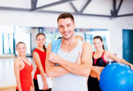 fitness, sport, training, gym and lifestyle concept - smiling man standing in front of the group of people in gym