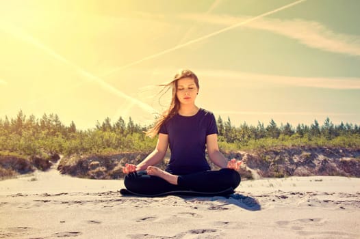 Young women practices yoga on the sand. 