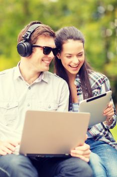 summer, internet, education, campus and teenage concept - students or teenagers with laptop and tablet computers hanging out