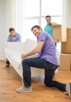 moving, real estate and friendship concept - smiling male friends with sofa and boxes at new home