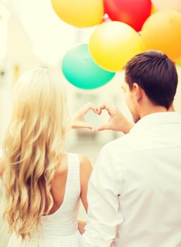 summer holidays, celebration and dating concept - couple with colorful balloons making heart shape in the city