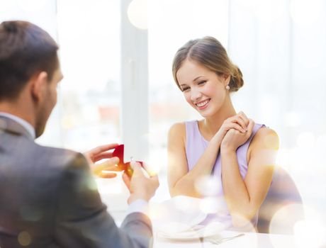 restaurant, couple and holiday concept - excited young woman looking at boyfriend with engagement ring at restaurant