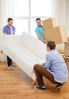 moving, real estate and friendship concept - smiling male friends with sofa and boxes at new home