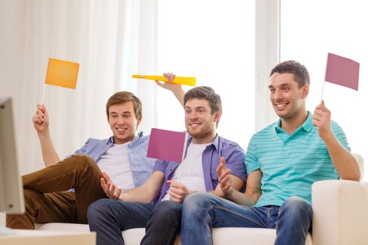 friendship, sports and entertainment concept - happy male friends with flags and vuvuzela supporting football team at home