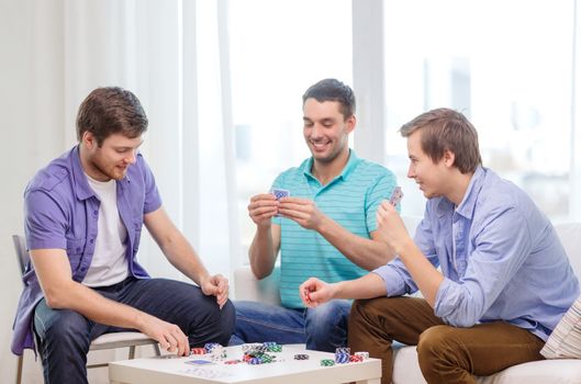 leisure, games and lifestyle concept - happy three male friends playing poker at home