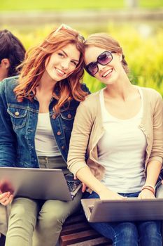 summer holidays, education, campus, technology and teenage concept - two female students with laptop computers