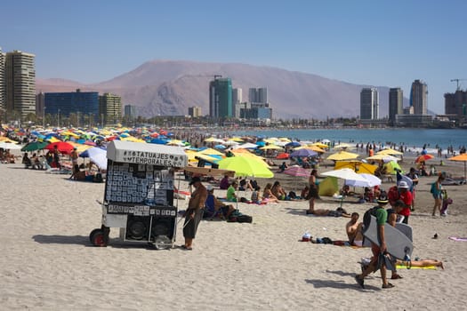 IQUIQUE, CHILE - JANUARY 23, 2015: Unidentified man pulling a cart through the sand offering temporal tattoos on the crowded Cavancha beach on January 23, 2015 in Iquique, Chile. Iquique is a popular beach town and free port city in Northern Chile.  