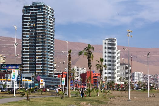 IQUIQUE, CHILE - JANUARY 23, 2015: Unidentified people walking along Arturo Prat Chacon avenue along the beach on January 23, 2015 in Iquique, Chile. Iquique is a popular beach town and free port city in Northern Chile. The red-blue building is the Arturo Prat University. 