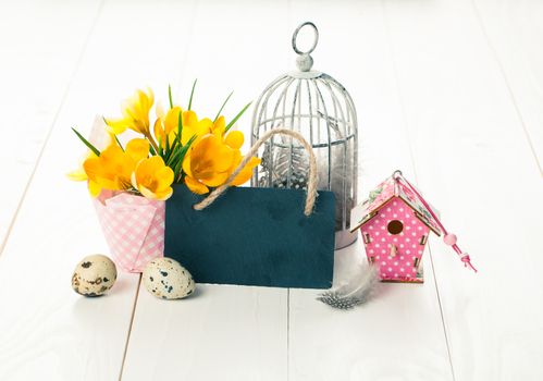 easter decoration with quail eggs, birdcage, yellow Spring Crocus, and blackboard, with space for text, on wooden white background.