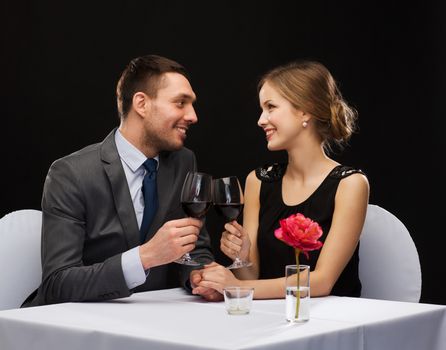 restaurant, couple and holiday concept - smiling young couple with glasses of red wine looking at each other at restaurant