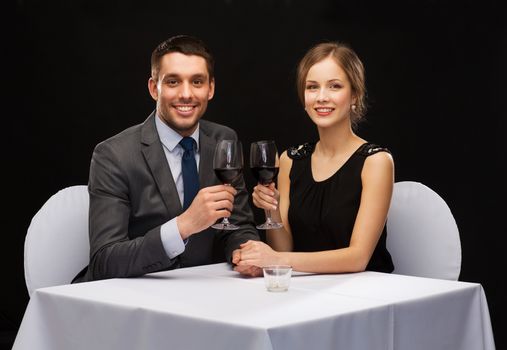 restaurant, couple and holiday concept - smiling young couple with glasses of red wine looking at each other at restaurant