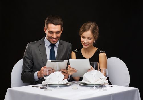 restaurant, couple, technology and holiday concept - smiling couple with menus on tablet pc computers at restaurant