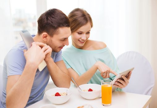 food, home, couple and technology concept - smiling couple with tablet pc reading news and having breakfast at home