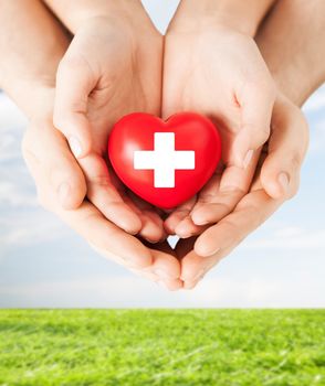 family health, charity and medicine concept - male and female hands holding red heart with cross sign