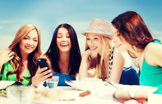 summer holidays, vacation and technology - girls looking at smartphone in cafe on the beach