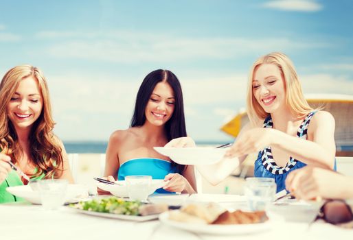 summer holidays and vacation - girls eating and drinking in cafe on the beach