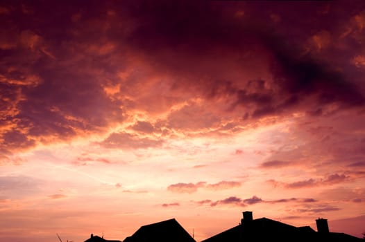 Sunset red sky with dark dramatic clouds over houses.