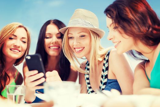 summer holidays, vacation and technology - girls looking at smartphone in cafe on the beach