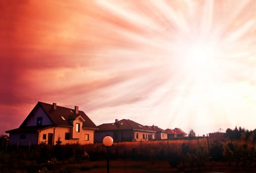 Sunset red sky with beams and dark dramatic clouds over houses.