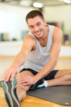 fitness, sport, training, gym and lifestyle concept - smiling man stretching on mat in the gym