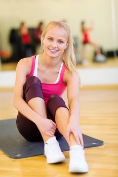 fitness, sport, training, gym and lifestyle concept - smiling woman stretching on mat in the gym