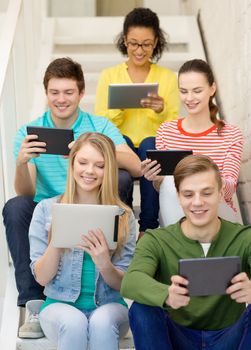 education and technology concept - smiling students with tablet pc computer sitting on staircase