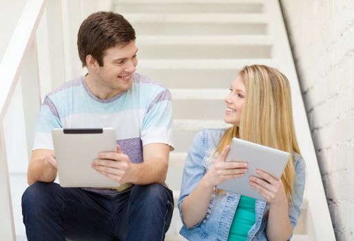 education and technology concept - smiling students with tablet pc computer sitting on staircase