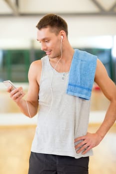 fitness, sport, training, gym, technology and lifestyle concept - young man with smartphone and towel in gym
